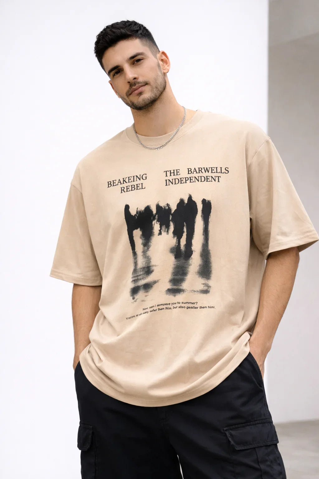 Man wearing beige graphic t-shirt with abstract black figures and text design, casual style