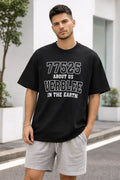 Man wearing black graphic oversized t-shirt with white text and gray shorts, standing outdoors