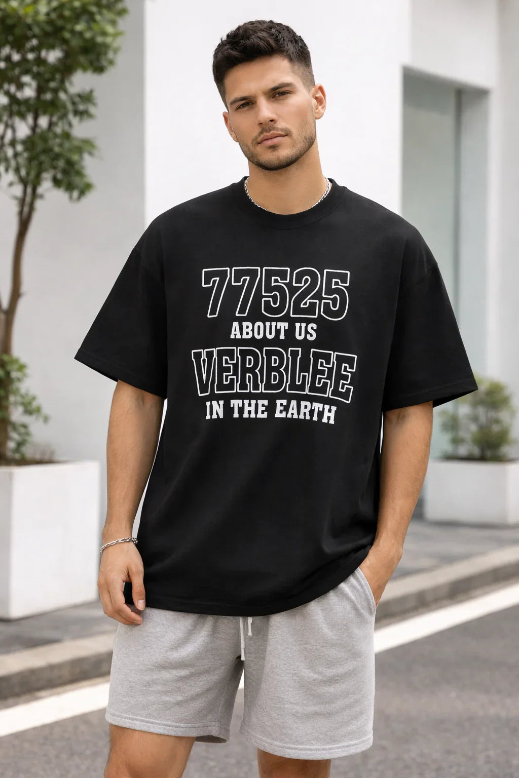 Man wearing black graphic oversized t-shirt with white text and gray shorts, standing outdoors