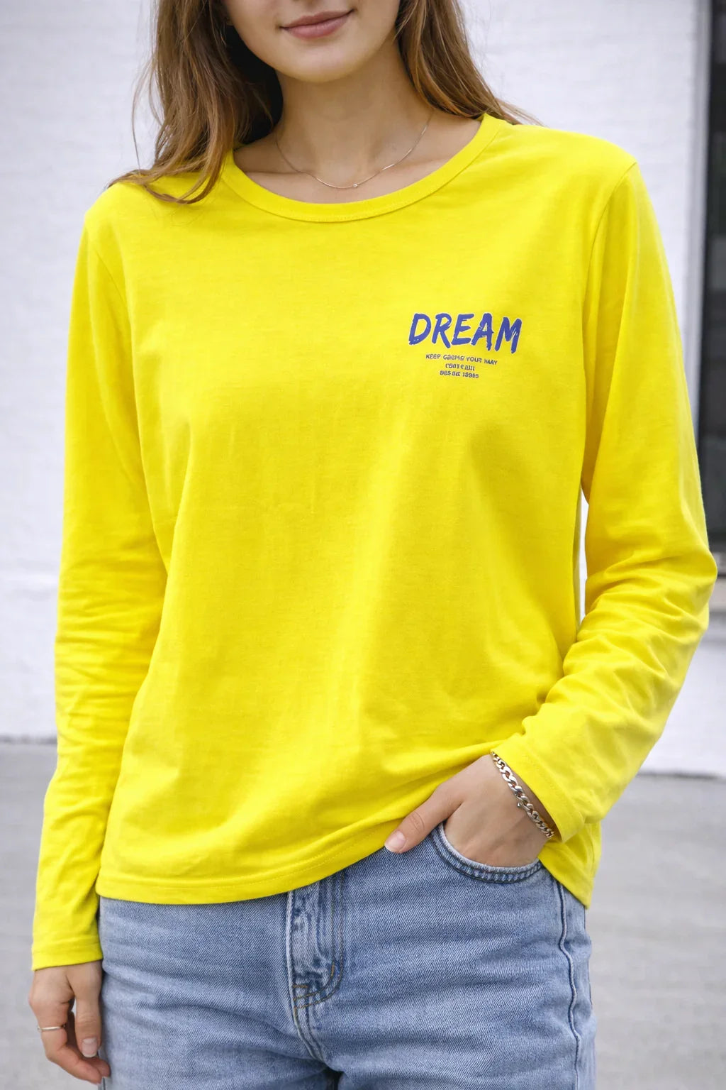 Woman in a bright yellow long sleeve t-shirt with 'DREAM' text, paired with blue jeans