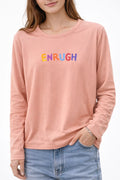 Woman wearing pink long sleeve t-shirt with colorful "ENRUGH" text graphic and blue jeans