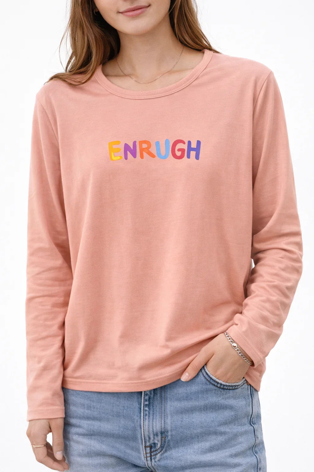 Woman wearing pink long sleeve t-shirt with colorful "ENRUGH" text graphic and blue jeans