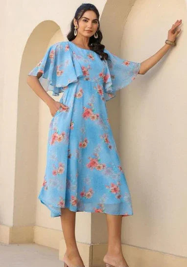 Woman wearing a blue floral midi dress with flutter sleeves, standing by an archway